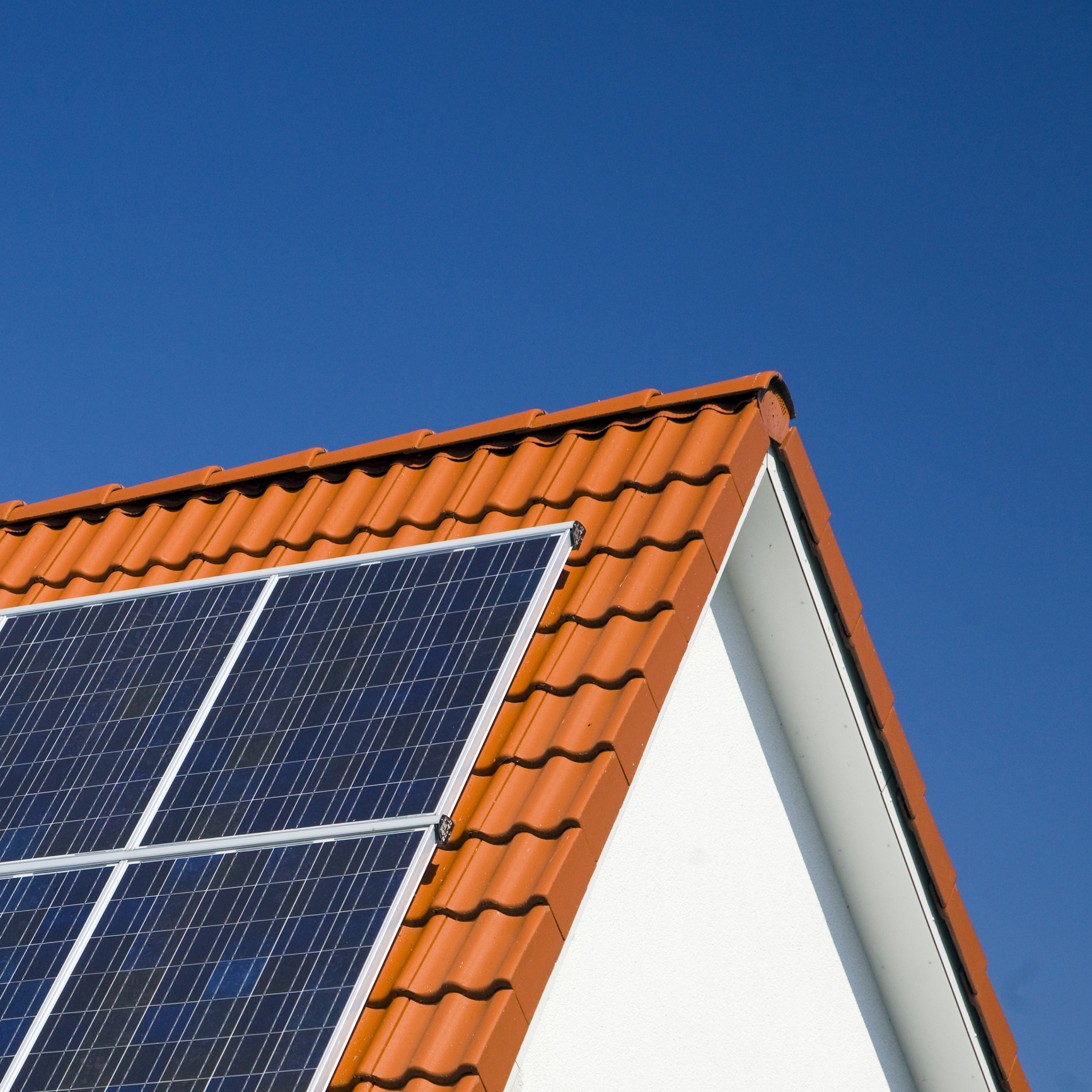 Corner of a pitched, red tiled roof with solar panels attached